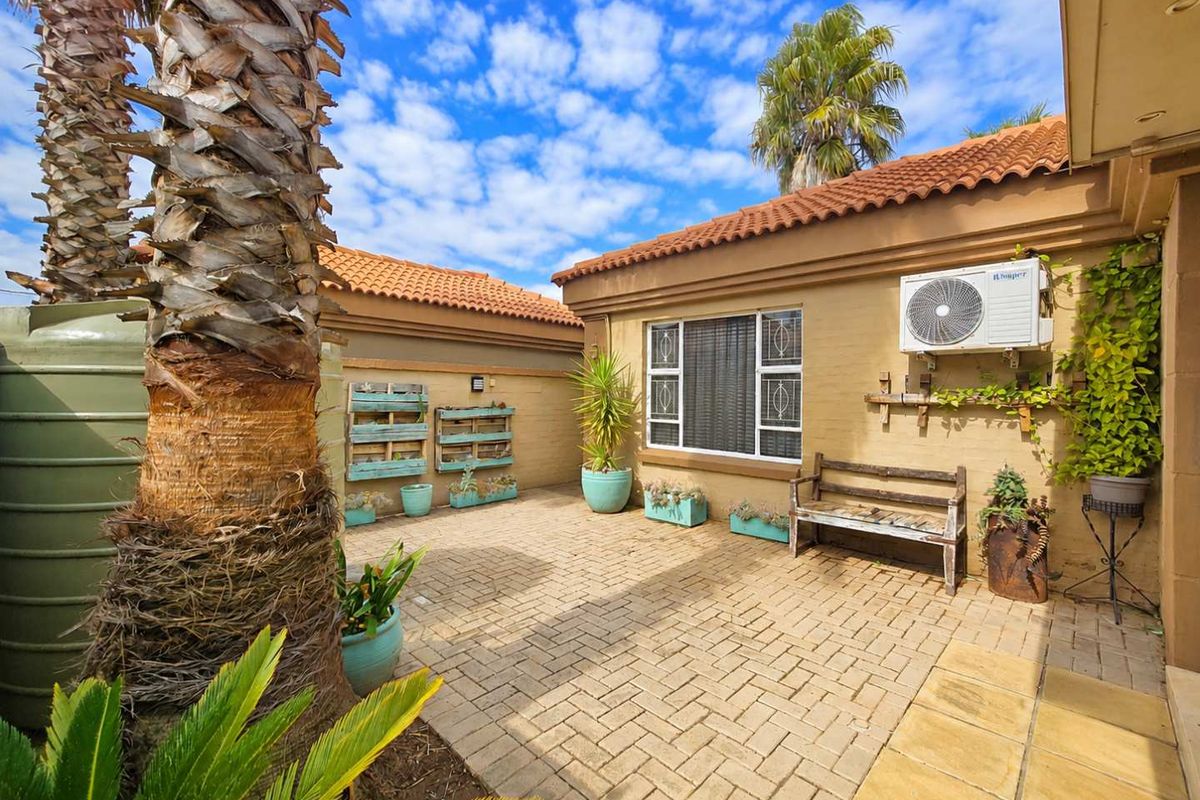 A well-maintained paved rear courtyard featuring a brick facade, security-barred windows, and an external air conditioning unit.