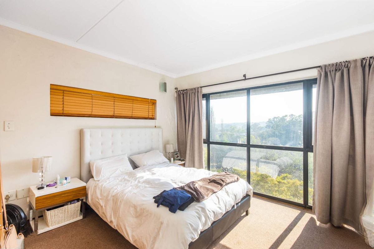 A bright bedroom featuring large floor-to-ceiling windows with natural light, neutral wall finishes, and carpeted flooring.