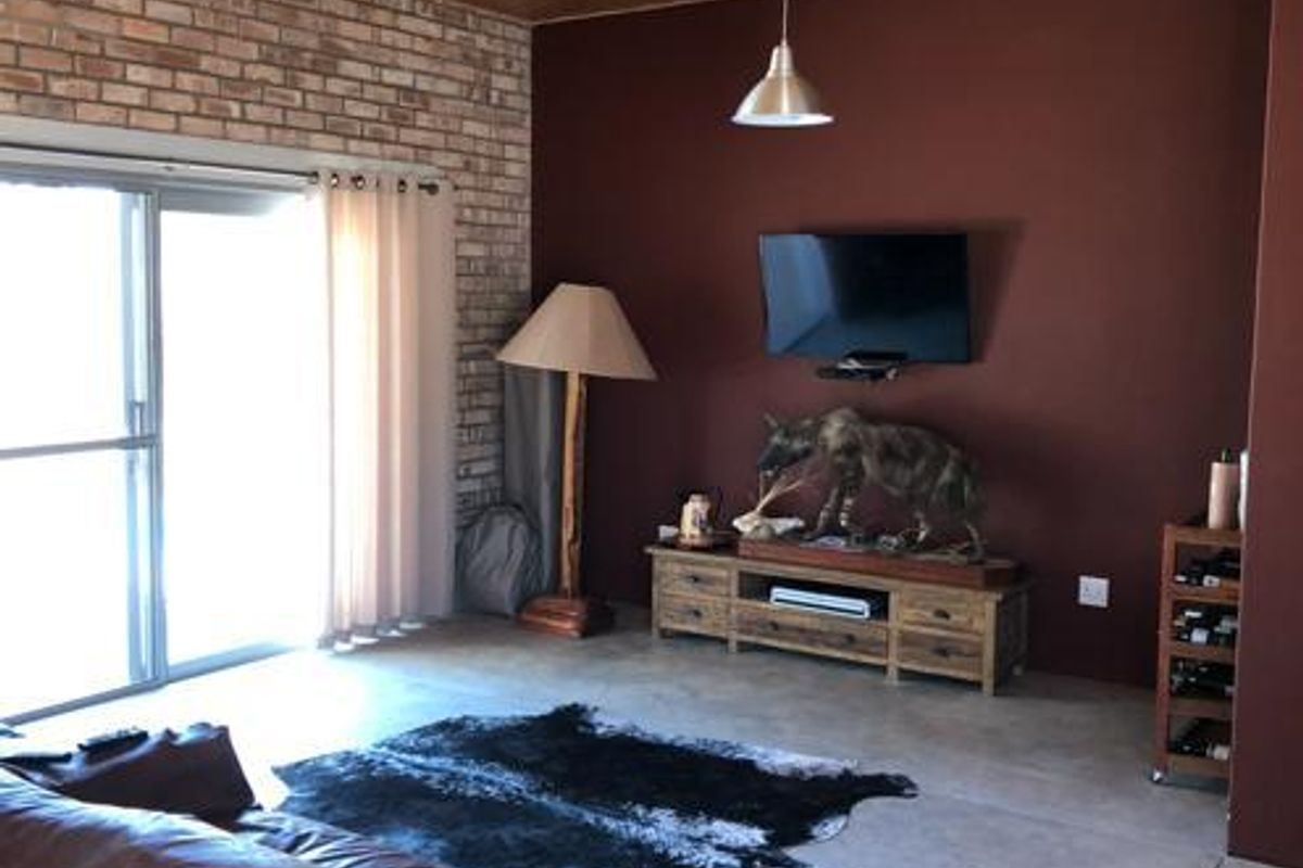 Living room featuring a unique OSB board ceiling, exposed brick wall, polished concrete floors, and large sliding glass doors providing natural light.