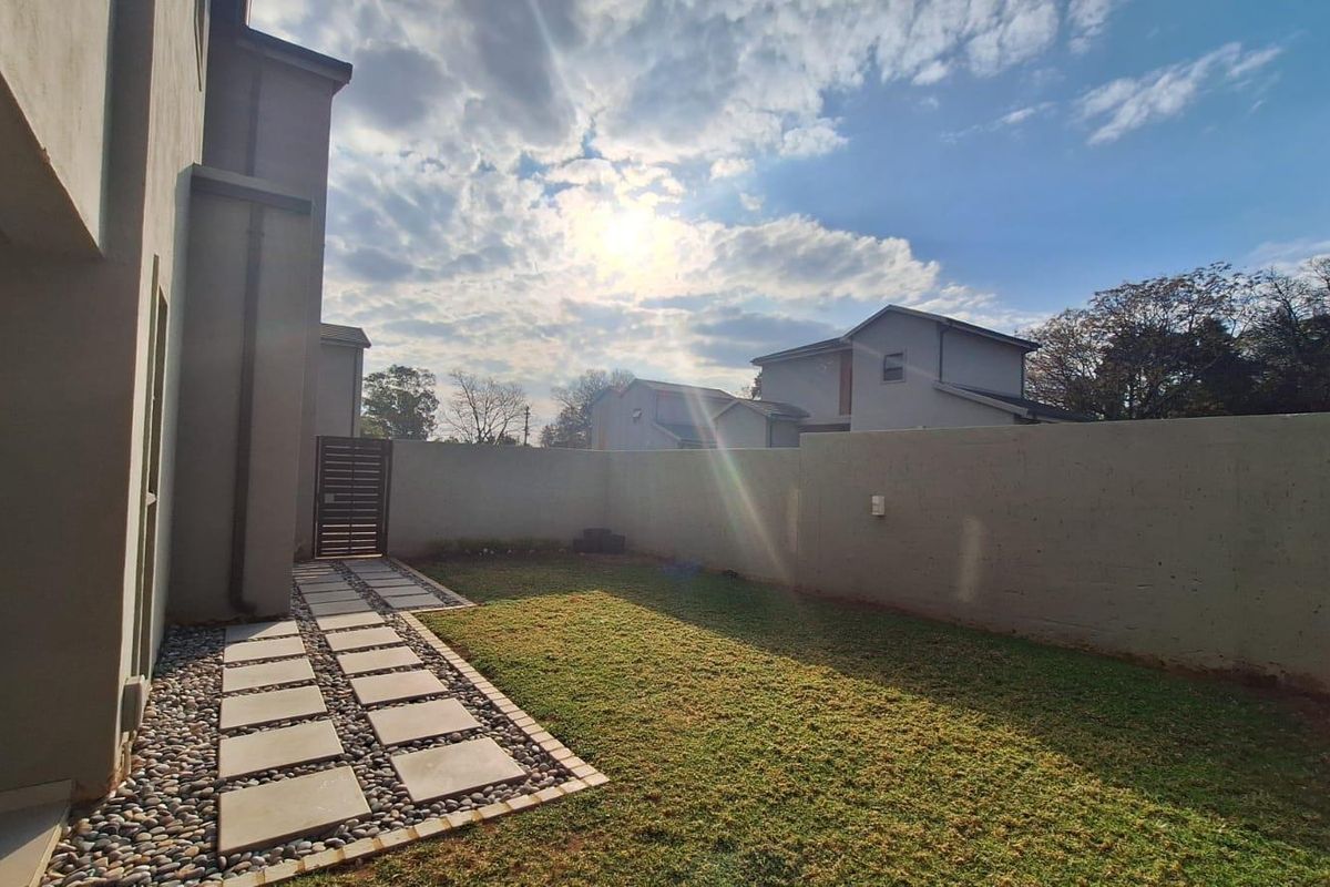 A private rear garden featuring a manicured lawn, a paved walkway with pebble detailing, and high boundary walls for added privacy.