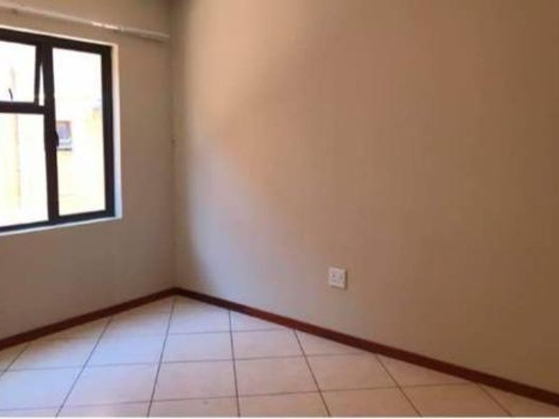 An empty bedroom featuring neutral wall paint, tiled flooring, and an aluminium-framed window.