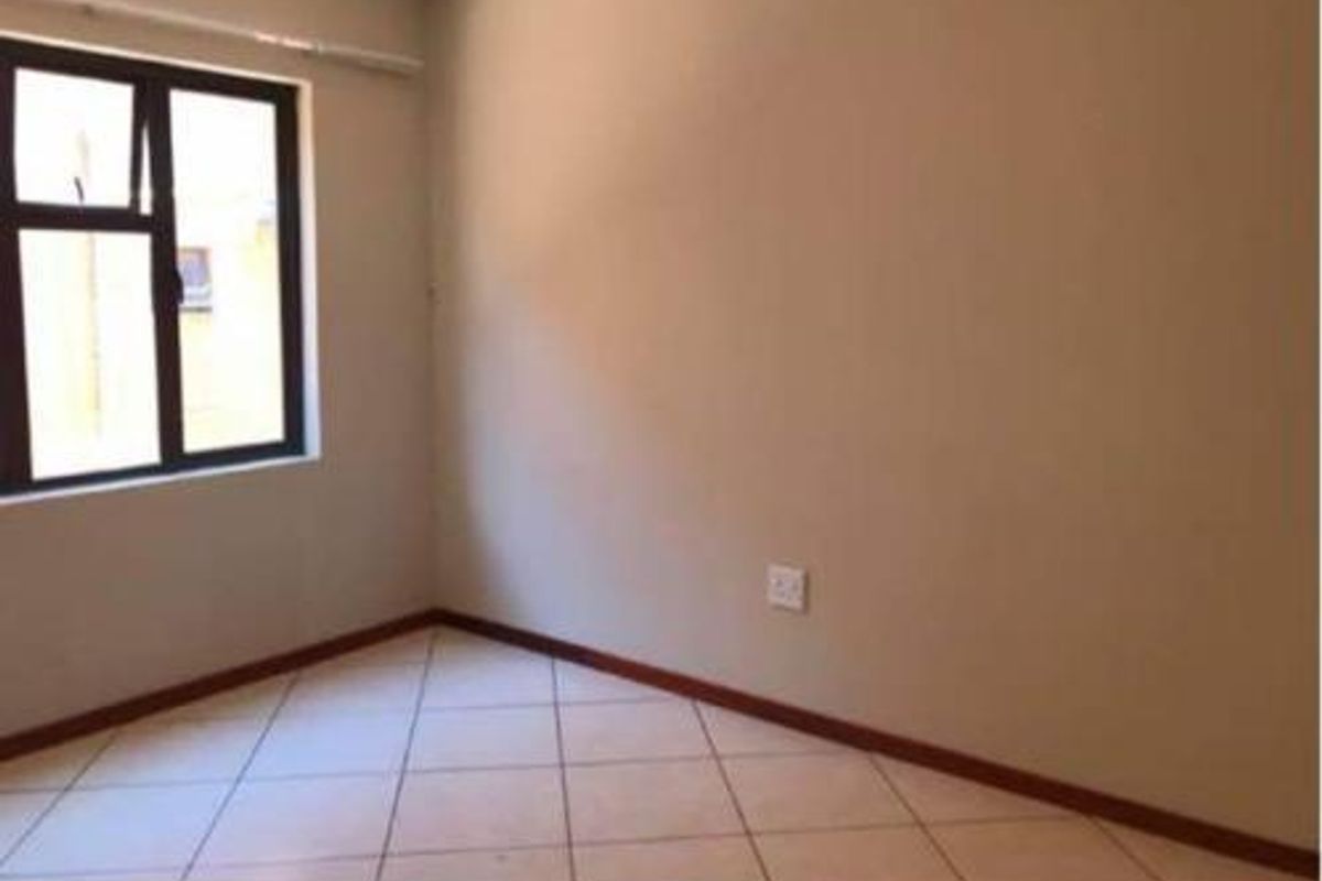 An empty bedroom featuring neutral wall paint, tiled flooring, and an aluminium-framed window.