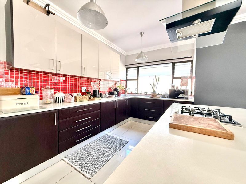 Modern kitchen featuring dark lower cabinetry, high-gloss upper cabinets, stone countertops, a gas hob with extractor, and a vibrant red tiled backsplash.