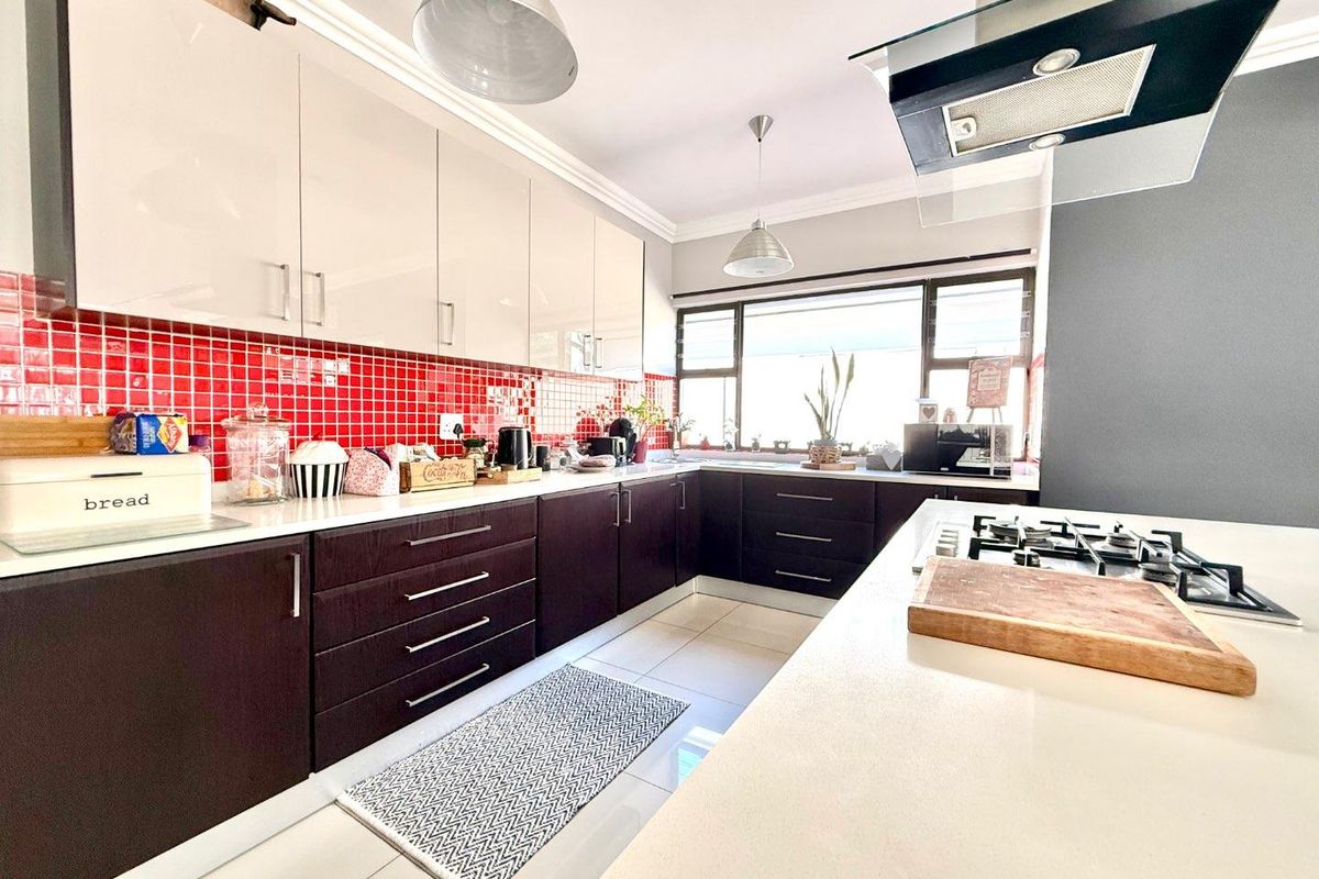 Modern kitchen featuring dark lower cabinetry, high-gloss upper cabinets, stone countertops, a gas hob with extractor, and a vibrant red tiled backsplash.