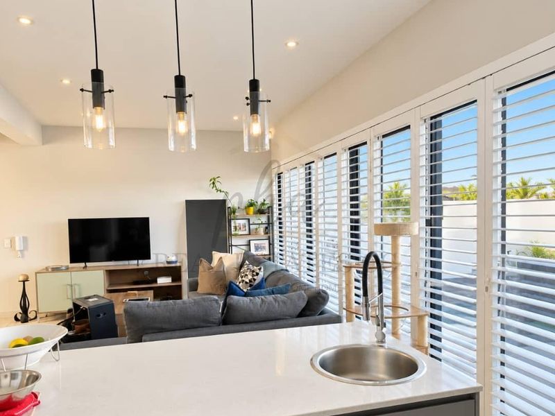 Modern open-plan living area featuring a sleek kitchen island with quartz countertop, pendant lighting, and large sliding doors with plantation shutters.