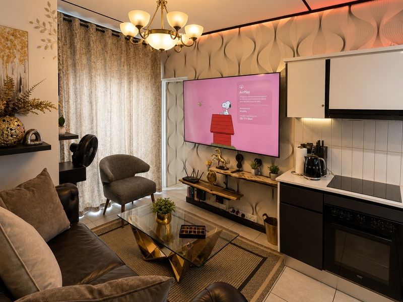 A compact open-plan living area featuring a modern kitchen with built-in appliances, tiled flooring, and a stylish chandelier, creating a functional and cozy space.