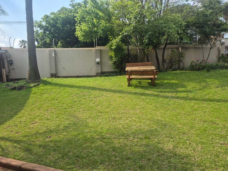 A private backyard garden featuring a well-maintained lawn, mature trees, and a perimeter boundary wall with integrated lighting.