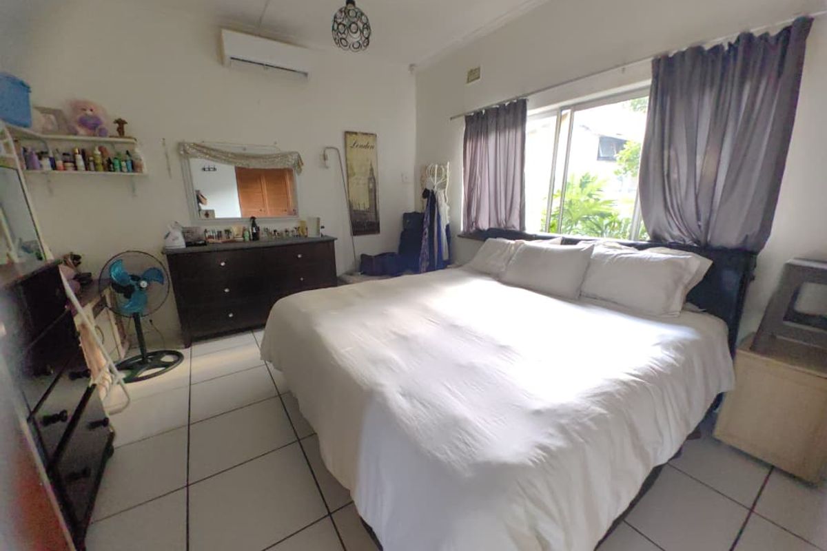 A spacious bedroom featuring tiled flooring, a wall-mounted air conditioning unit, and large windows allowing for natural light.