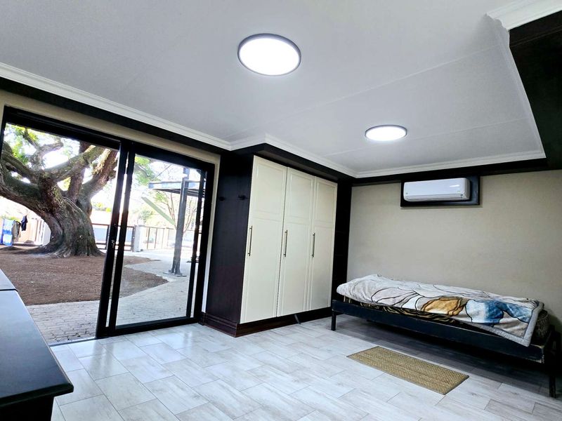 A well-maintained bedroom featuring built-in cupboards, air conditioning, modern tiled flooring, and a large sliding glass door providing access to the garden.