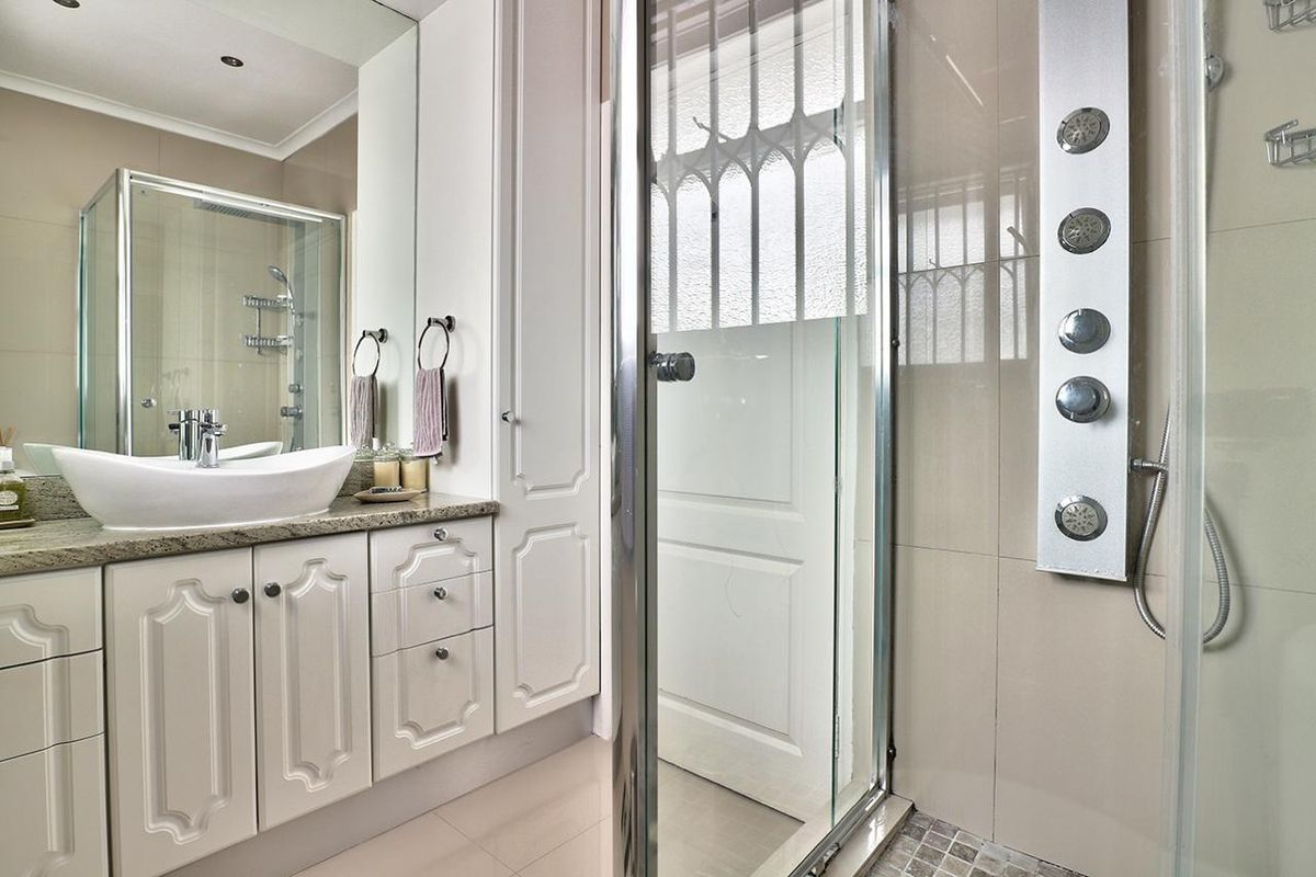 Modern bathroom featuring a vanity with granite countertop, vessel sink, large mirror, and a glass-enclosed shower with a multi-jet shower panel.