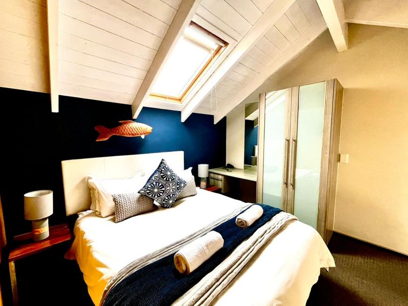 Cozy attic-style bedroom featuring a skylight, exposed timber ceiling beams, and integrated built-in cabinetry including a wardrobe and vanity desk.