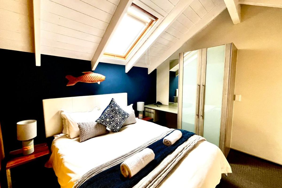 Cozy attic-style bedroom featuring a skylight, exposed timber ceiling beams, and integrated built-in cabinetry including a wardrobe and vanity desk.