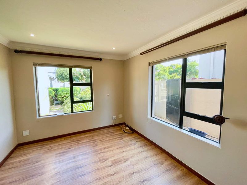 A bright, empty bedroom featuring laminate flooring, aluminium window frames, and recessed downlighting, offering a clean canvas for interior design.