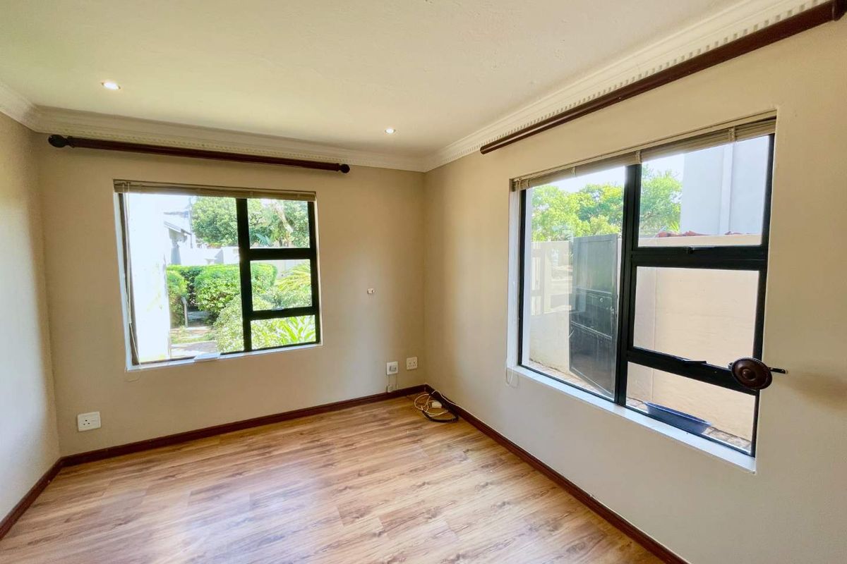 A bright, empty bedroom featuring laminate flooring, aluminium window frames, and recessed downlighting, offering a clean canvas for interior design.