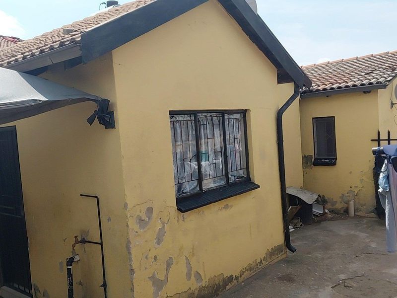Rear exterior view of a residential property showing yellow painted walls with visible plaster damage and peeling paint, tiled roofing, and security window bars.