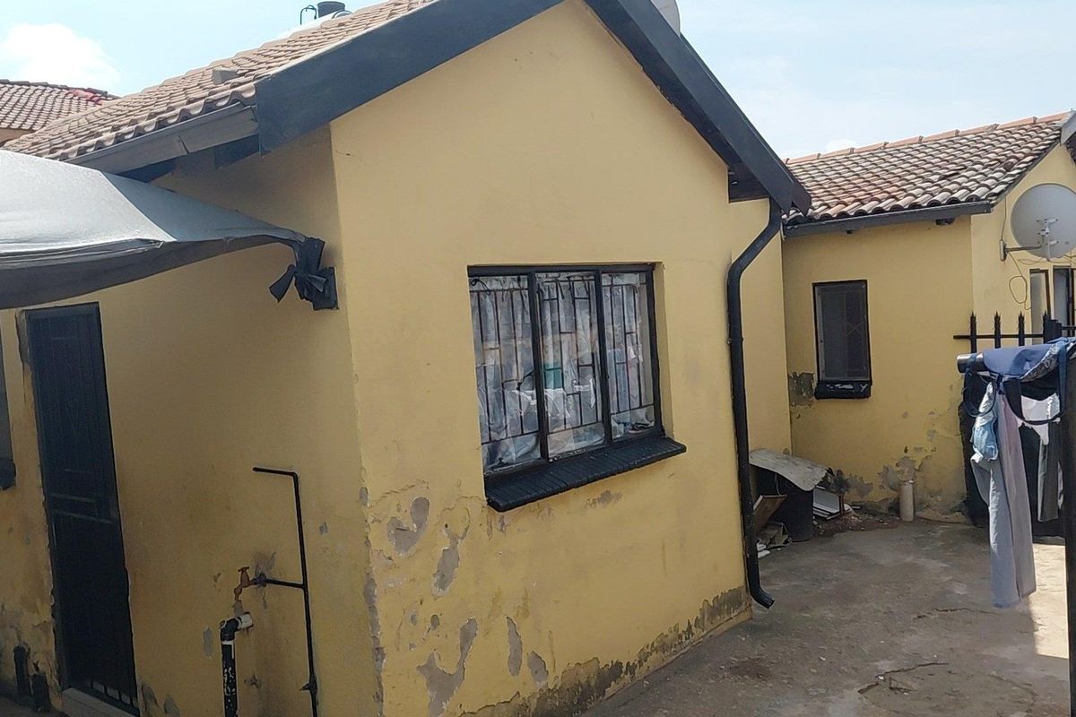 Rear exterior view of a residential property showing yellow painted walls with visible plaster damage and peeling paint, tiled roofing, and security window bars.