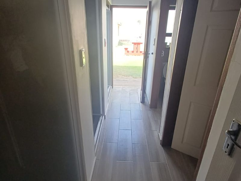 A functional hallway featuring light-toned tiled flooring, connecting multiple rooms and leading to an exterior exit.