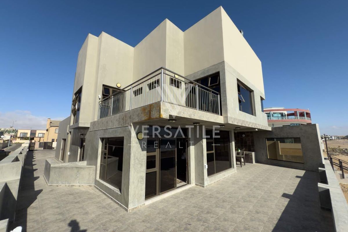 Modern two-story residence featuring a spacious tiled patio, upper-level balcony with metal railings, and large dark-framed windows.