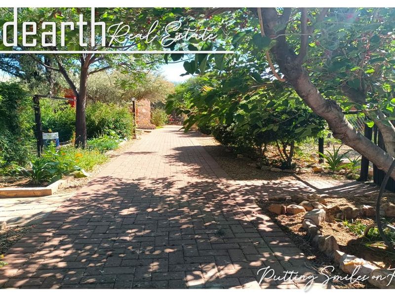 A well-maintained garden pathway featuring brick paving, mature trees, and established garden beds within the retirement village grounds.