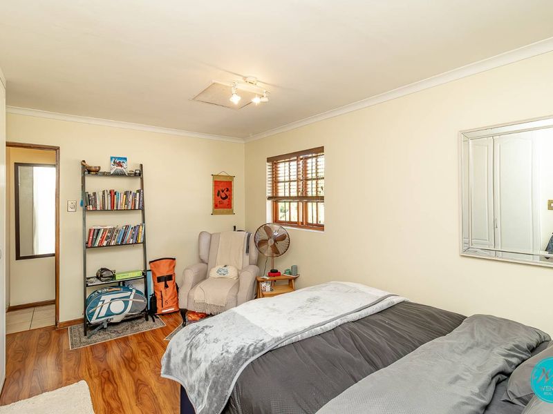 A comfortable bedroom featuring timber laminate flooring, built-in wardrobe storage, and natural light through timber venetian blinds.