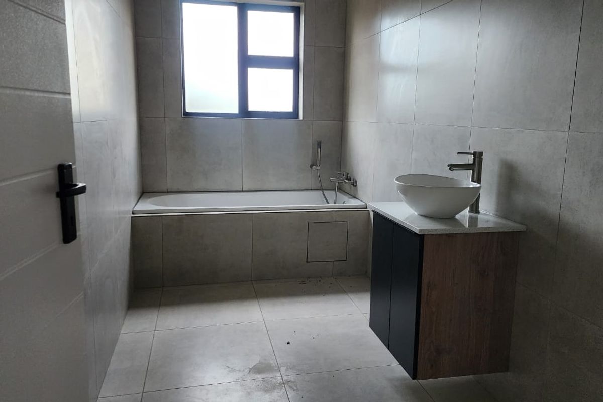 A modern, minimalist bathroom featuring large-format wall and floor tiles, a built-in bathtub, and a contemporary wall-mounted vanity with a vessel sink.