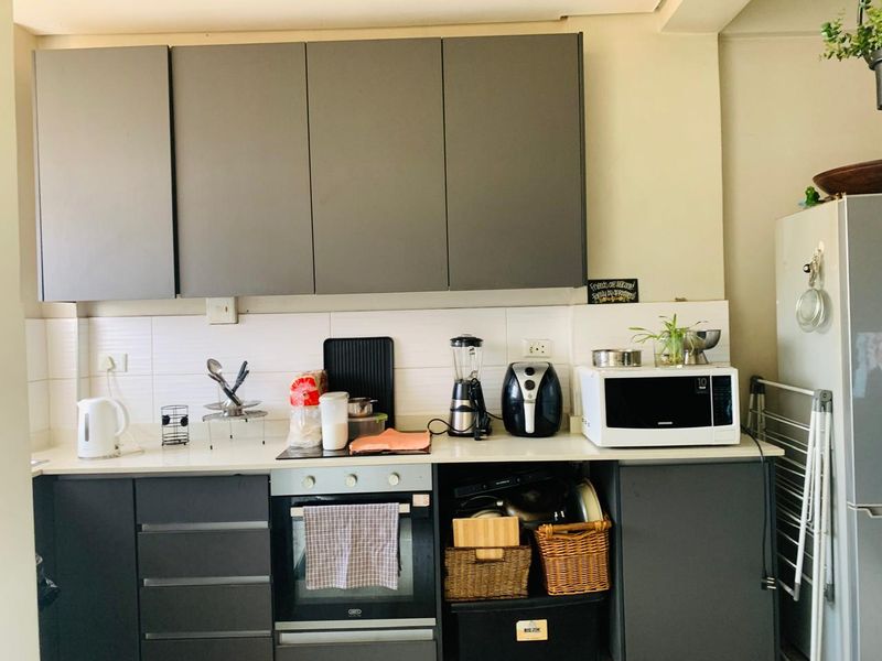 A functional kitchen featuring grey cabinetry, a white tiled backsplash, and integrated oven and hob, providing a clean and practical cooking space.