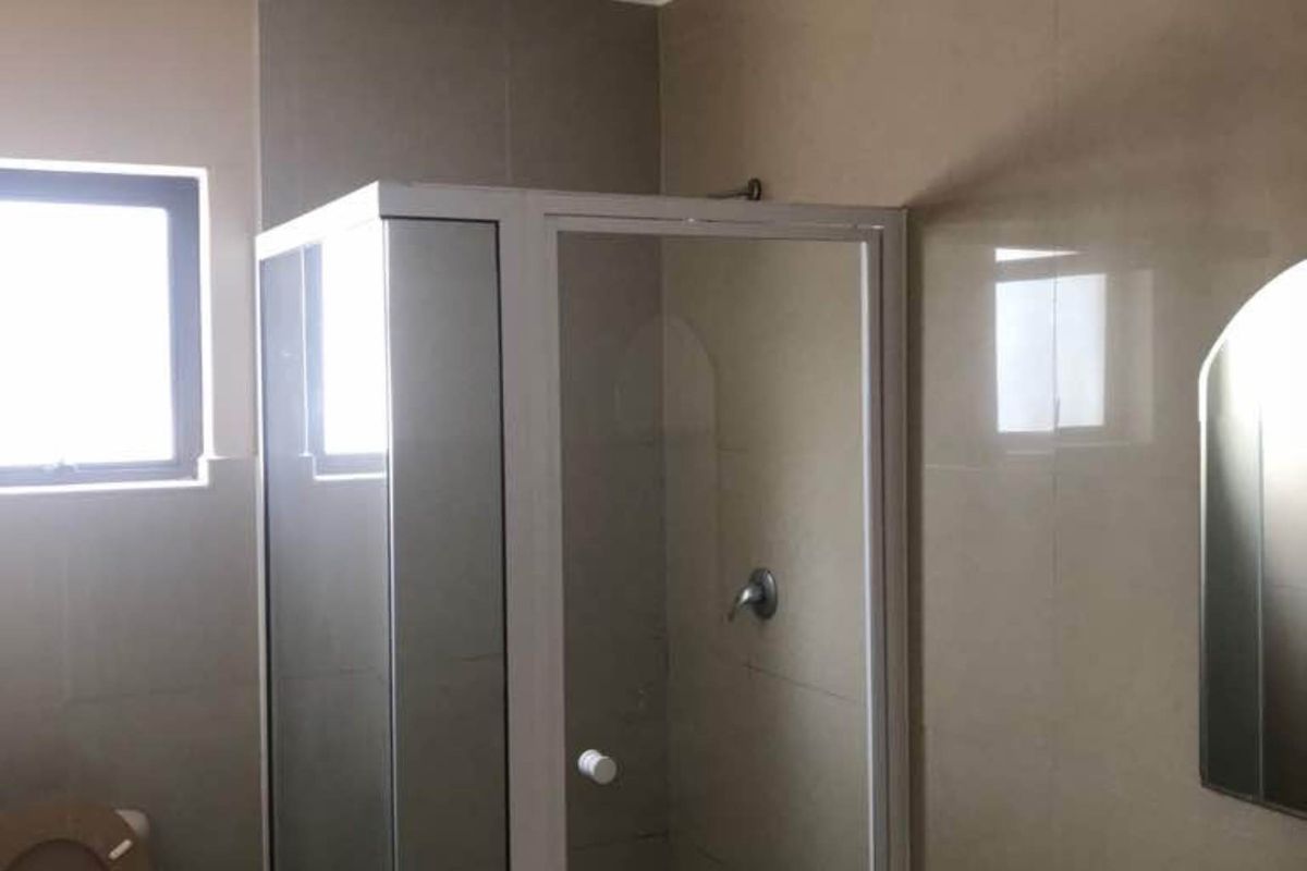 A functional bathroom featuring a glass-enclosed shower, pedestal basin, and toilet with neutral wall tiling and a flush-mount ceiling light.