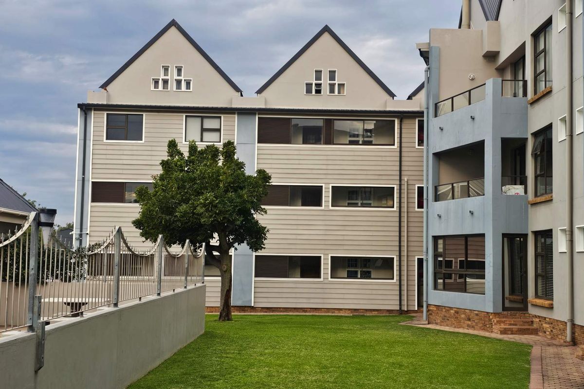 Rear view of a multi-story apartment complex featuring landscaped lawn, paved walkways, and private balconies.