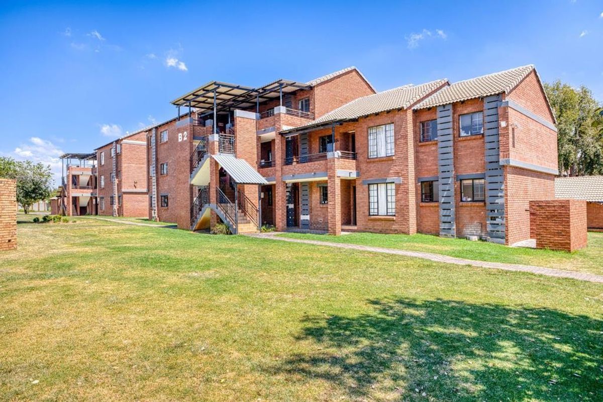 Exterior view of a multi-story face brick apartment complex featuring balconies, metal staircases, and surrounding landscaped lawn areas.