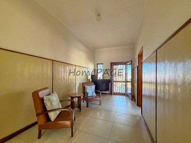 A spacious hallway featuring tiled flooring and decorative wall paneling, leading to an exterior entrance with a security gate.