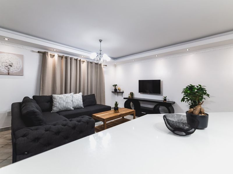 A well-maintained open-plan living area featuring recessed ceiling lighting, decorative cornicing, and neutral tiled flooring, creating a bright and inviting space.