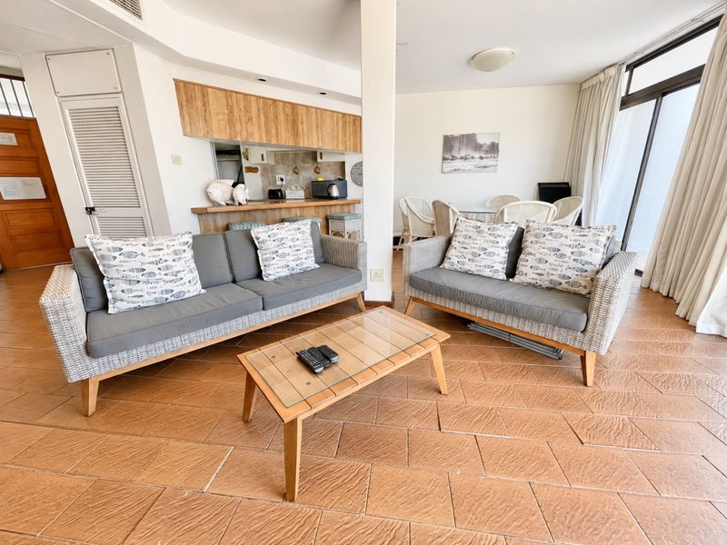 Open-plan living and kitchen area featuring terracotta floor tiles, a breakfast bar, and direct access to a balcony through sliding glass doors.