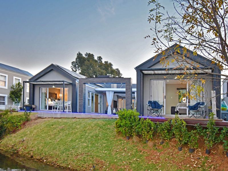Rear view of modern residential units featuring timber decking, sliding glass doors, and a connecting pergola structure overlooking a landscaped garden and water feature.