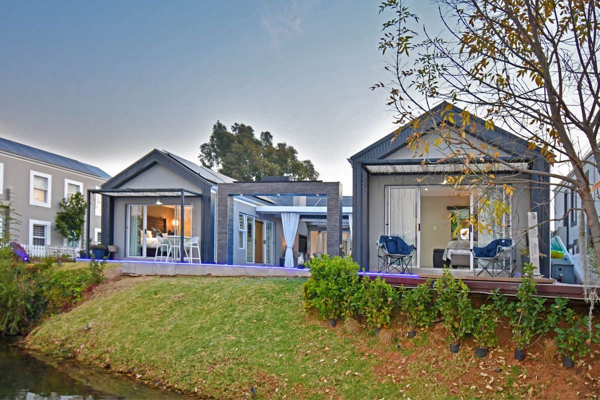 Rear view of modern residential units featuring timber decking, sliding glass doors, and a connecting pergola structure overlooking a landscaped garden and water feature.
