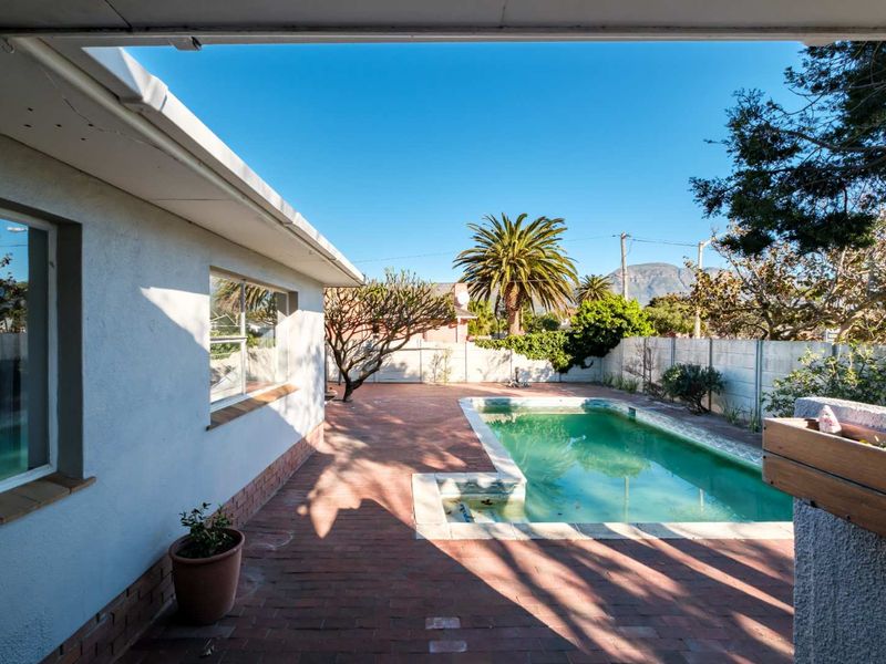 Rear garden area featuring a swimming pool, brick paved patio, and perimeter boundary wall, viewed from a covered patio space.