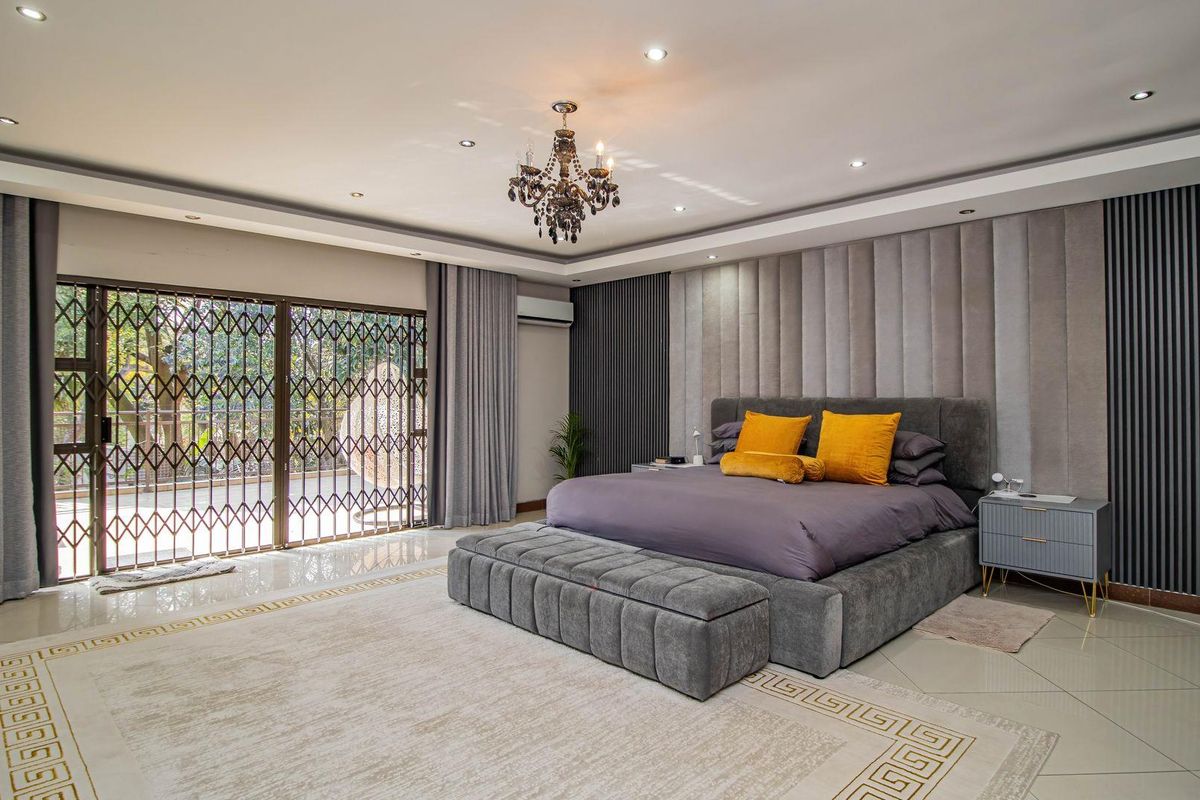 Spacious primary bedroom featuring a modern upholstered feature wall, recessed ceiling lighting, tiled flooring, and large sliding doors with security gates leading outdoors.