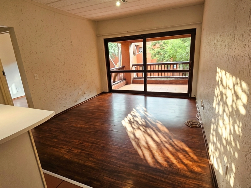 An open-plan living area featuring dark laminate flooring, textured walls, and a sliding glass door leading to a private balcony.