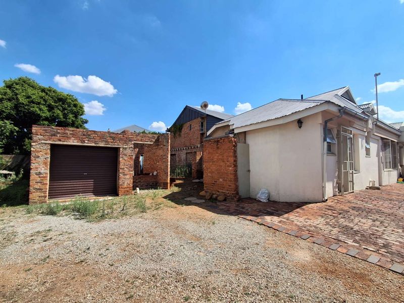 Rear exterior view showing a brick garage structure, paved area, and main building facade with visible maintenance and completion requirements.