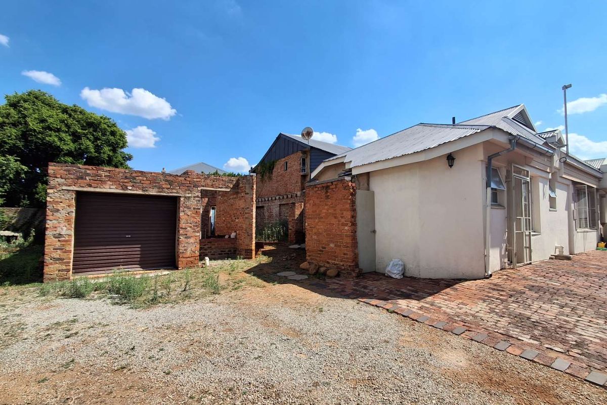 Rear exterior view showing a brick garage structure, paved area, and main building facade with visible maintenance and completion requirements.