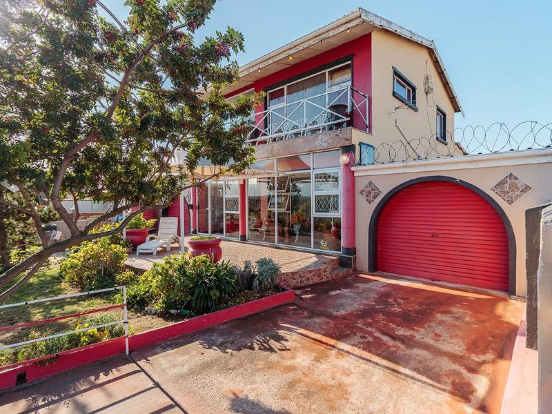 Front elevation of a multi-level house featuring a red roller garage door, a tiled patio area, and an upper-level balcony with security fencing.