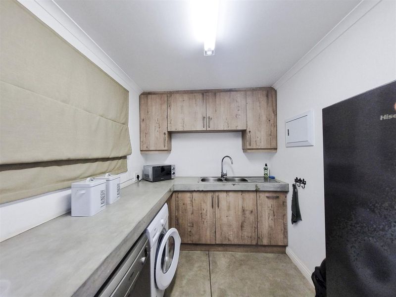 A functional laundry room featuring concrete countertops, double bowl sink, and wood-look laminate cabinetry with ample storage space.