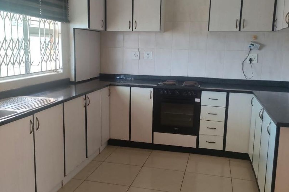 A functional kitchen featuring white cabinetry, dark countertops, built-in oven and hob, and tiled flooring, offering a clean canvas for potential modern updates.