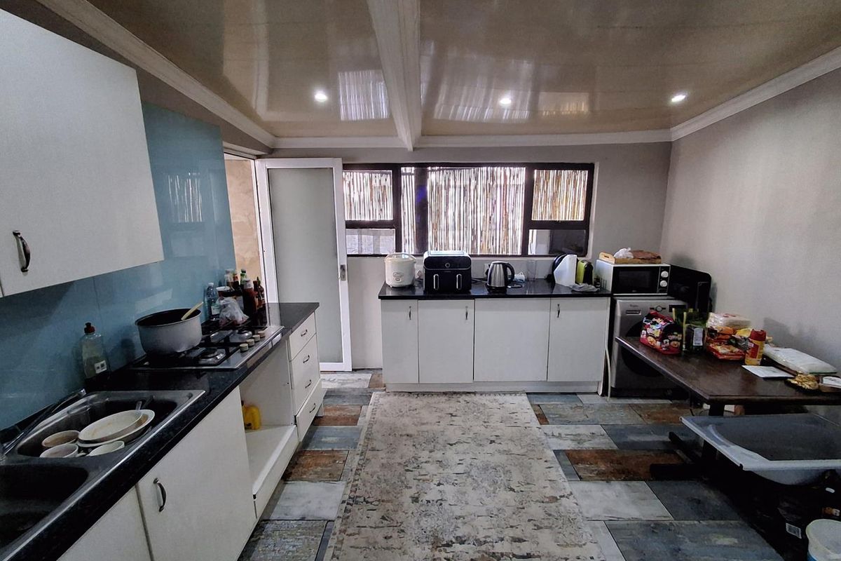 A functional kitchen featuring white cabinetry, granite countertops, a gas hob, and tiled flooring, offering a practical layout for daily meal preparation.