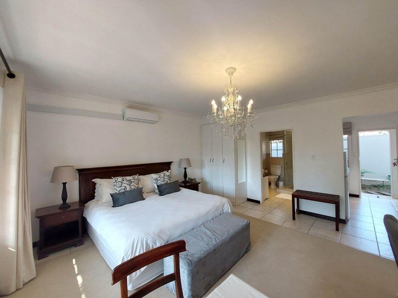 Spacious bedroom featuring built-in cupboards, a split-system air conditioner, and an attached en-suite bathroom with tiled flooring.