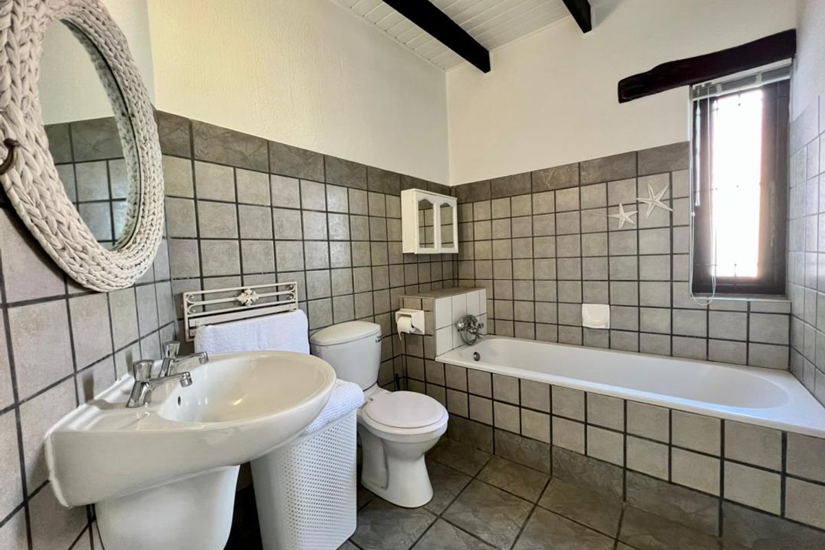 A functional bathroom featuring a pedestal washbasin, toilet, and built-in bathtub with neutral tiled walls and exposed ceiling beams.