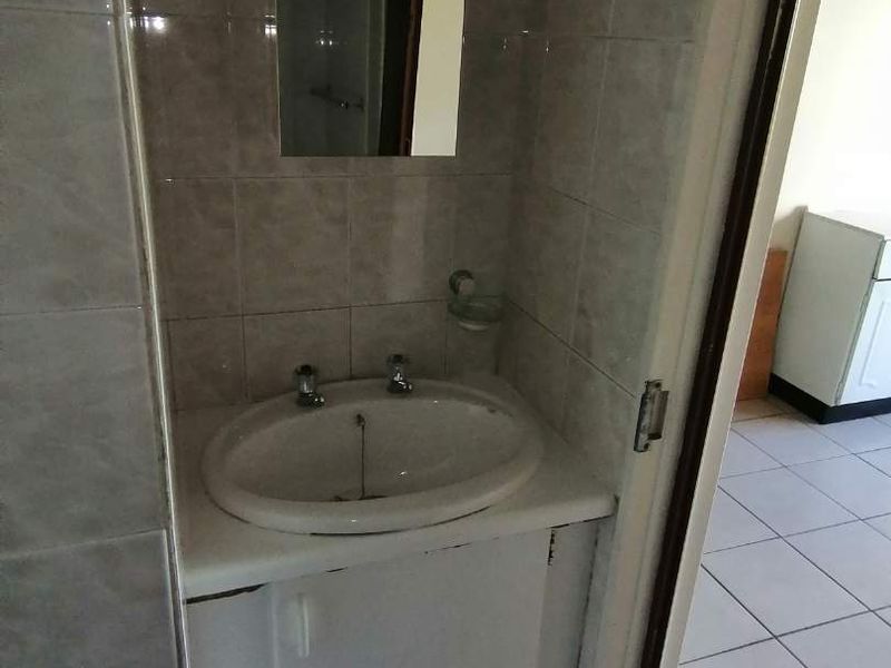 A compact bathroom featuring a built-in vanity cabinet with a ceramic basin and wall-mounted mirror, finished with neutral wall and floor tiles.