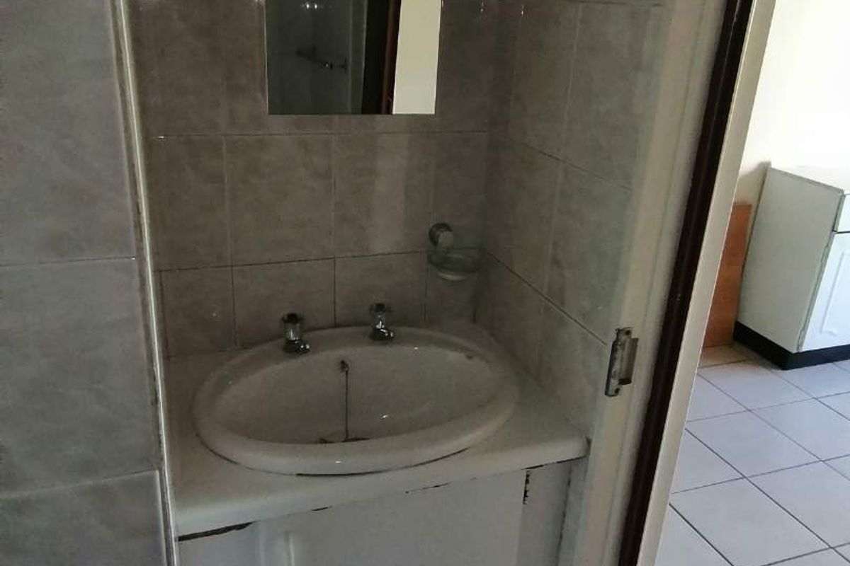 A compact bathroom featuring a built-in vanity cabinet with a ceramic basin and wall-mounted mirror, finished with neutral wall and floor tiles.