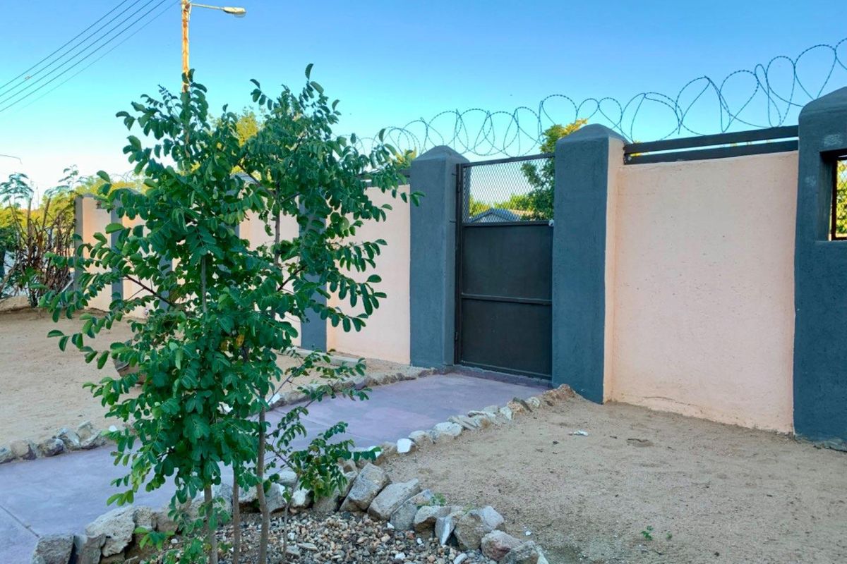 A secure perimeter boundary wall featuring a metal pedestrian gate, topped with razor wire for enhanced security.