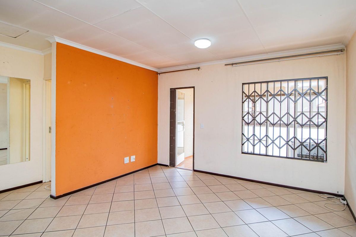 An empty living room featuring tiled flooring, a security gate on the window, and a prominent orange accent wall.