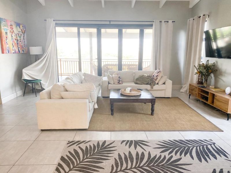 Spacious living room featuring tiled floors, exposed beam ceilings, and large sliding glass doors that provide access to the outdoor patio area.